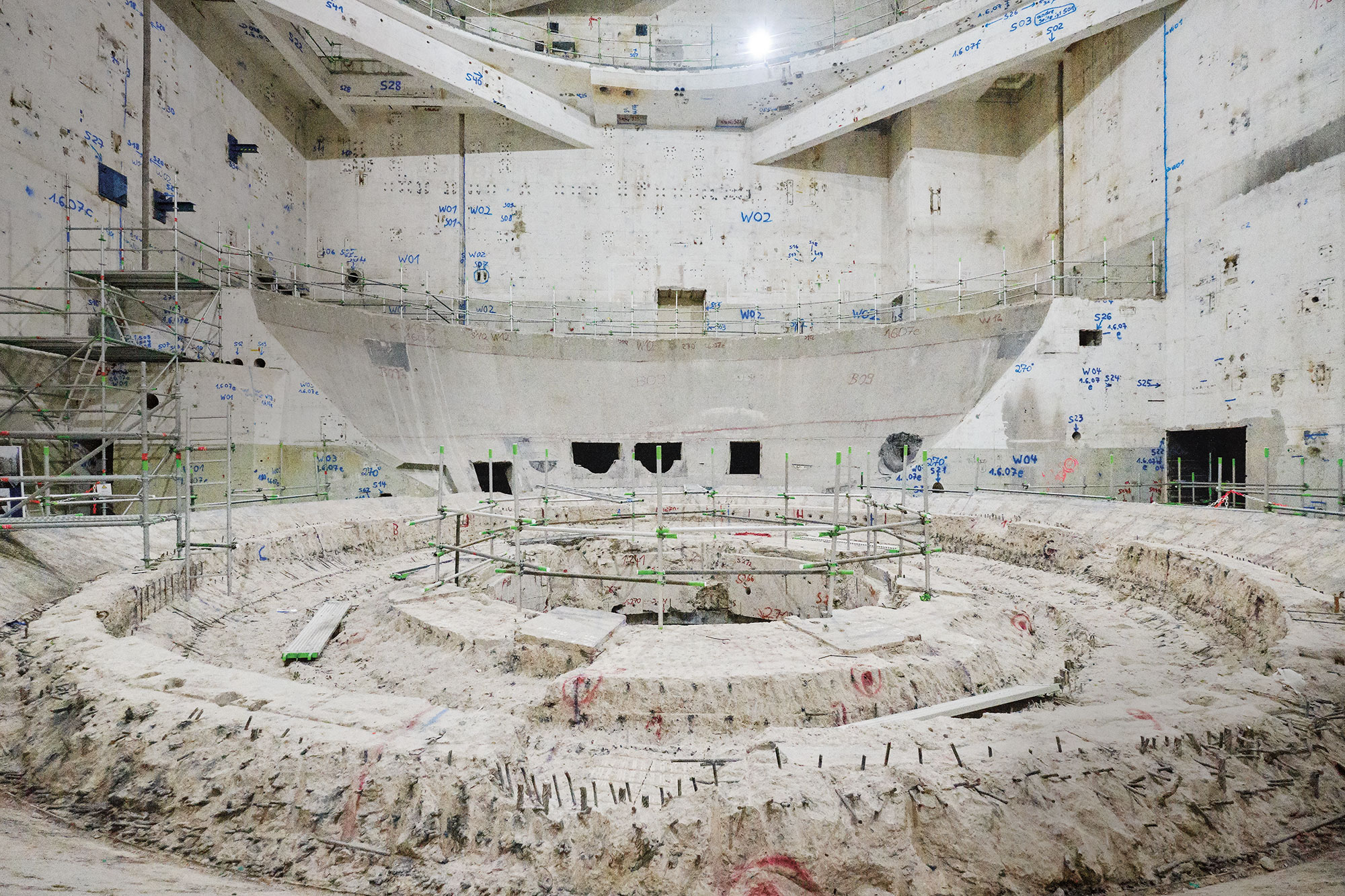 Das Foto zeigt einen großen Raum aus hellem Beton. In der Mitte befinden sich kreisrunde Fundamentreste.